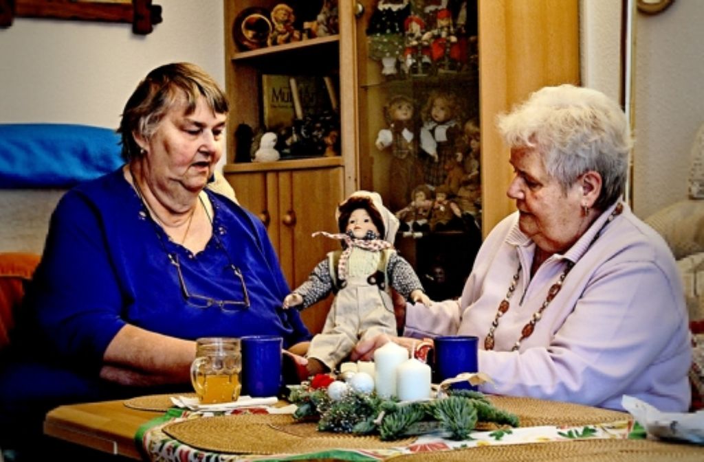 Karin Volle (links) zeigt ihrer Besucherin Lilli Fleck eine der   Puppen aus ihrer umfangreichen Sammlung, die zwei Vitrinen im Wohnzimmer füllen. Foto: factum/Granville