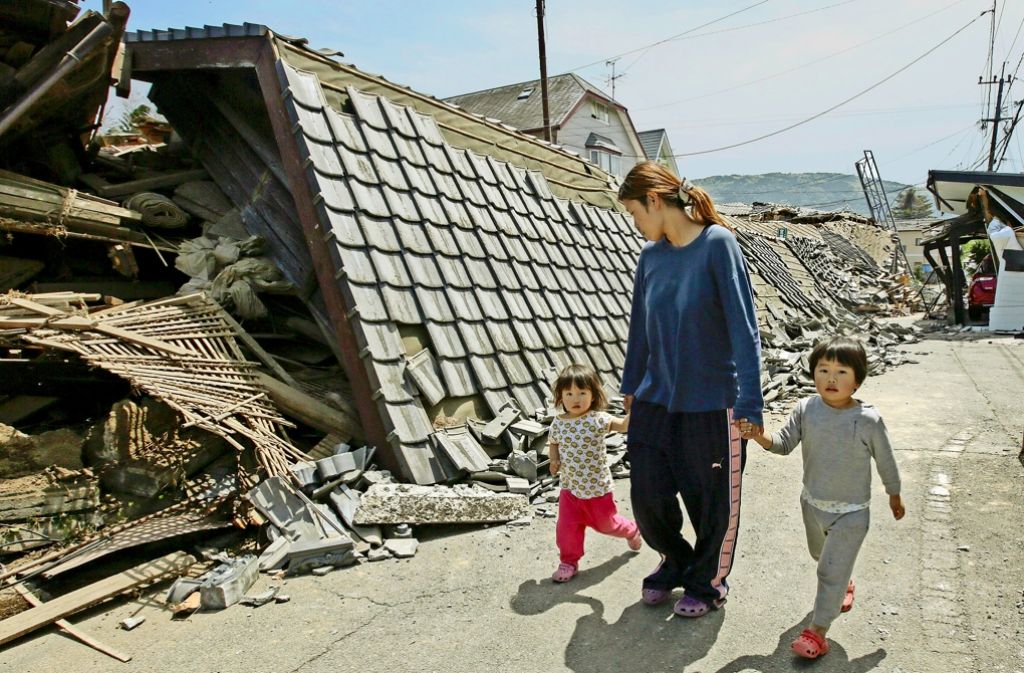 Eine Mutter geht mit ihren zwei Kindern durch eine vom Erdbeben zerstörte Straße in der Präfektur Kumamoto. Foto: dpa