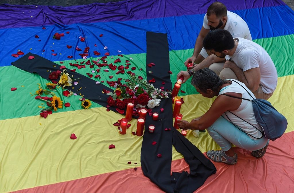 In Barcelona zünden Trauernde Kerzen auf einer Regenbogenflagge an.