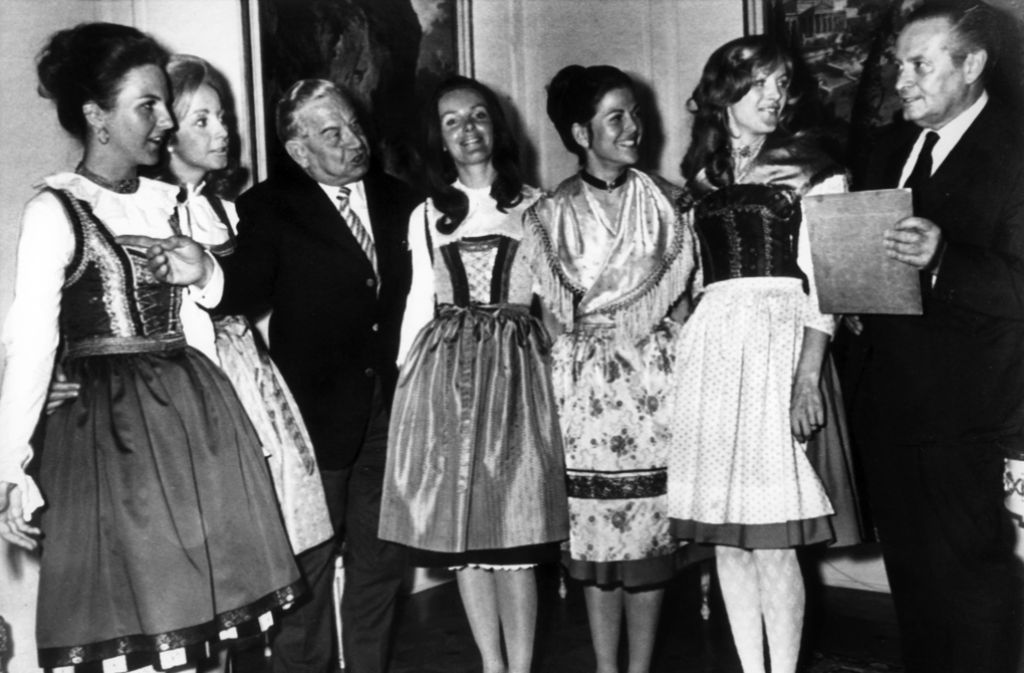 Die spätere Königin Silvia von Schweden (3.v.r.) zeigt gemeinsam mit anderen Hostessen dem bayerischen Ministerpräsidenten Alfons Goppel (l.) und dem deutschen NOK-Präsident Willi Daume (r.) in 1972 in München die bayerischen Trachten, in denen die Mädchen bei den Olympischen Spielen 1972 in München die Medaillen überreichen werden.