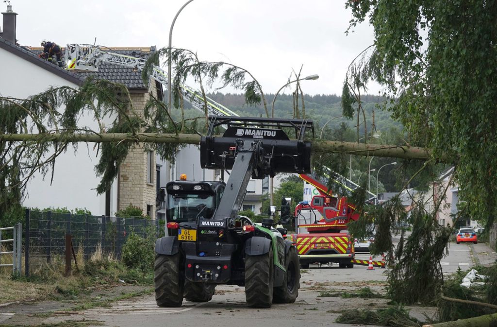 Petingen: Nach einem schweren Unwetter mit einem Tornado räumen Helfer einen umgestürzten Baum von einer Straße.
