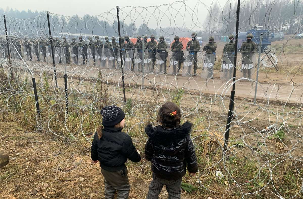 Kein Durchkommen. Kinder stehen in einem Flüchtlingslager nahe der belarussisch-polnischen Grenze. Auf der anderen Seite des Zaunes verhindern polnische  Soldaten, dass die Migranten die Grenze überschreiten. Foto: dpa/Henadz Zhinkov