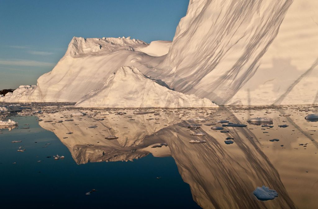 Die Mitternachtssonne leuchtet golden auf einem Eisberg und spiegelt sich in der Disko Bay, Grönland.