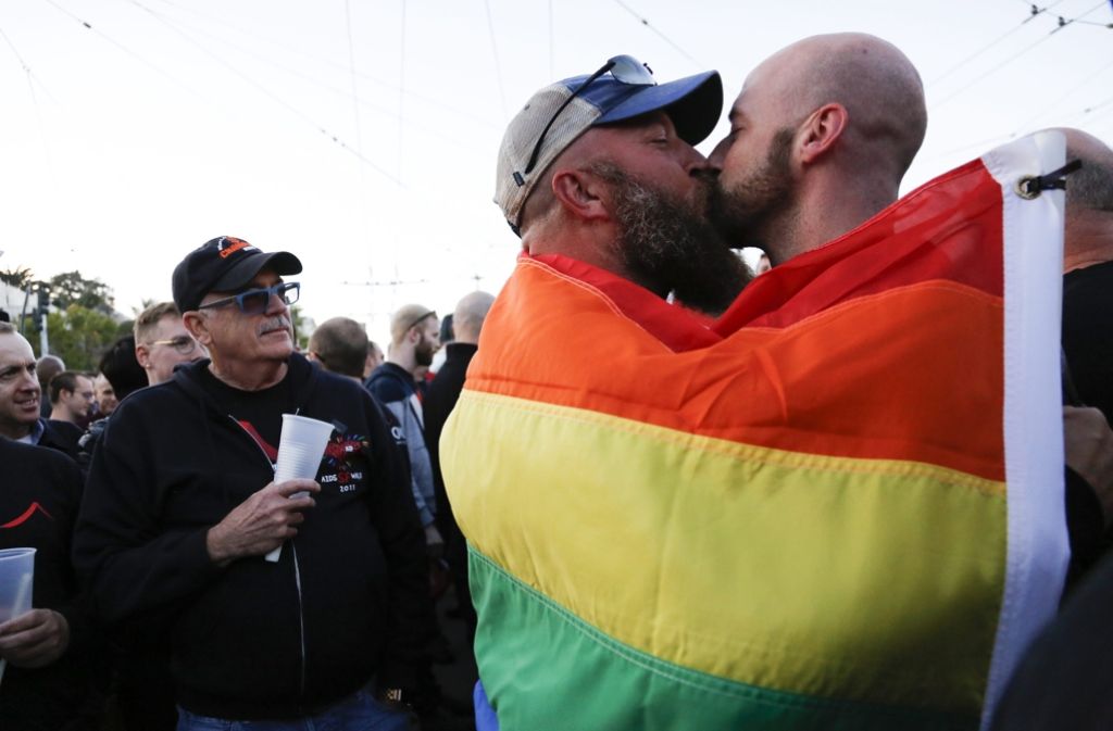 Ein Paar küsst sich während einer Trauerfeier in San Francisco – eingehüllt in eine Regenbogen-Flagge, die für Vielfalt und Frieden steht.
