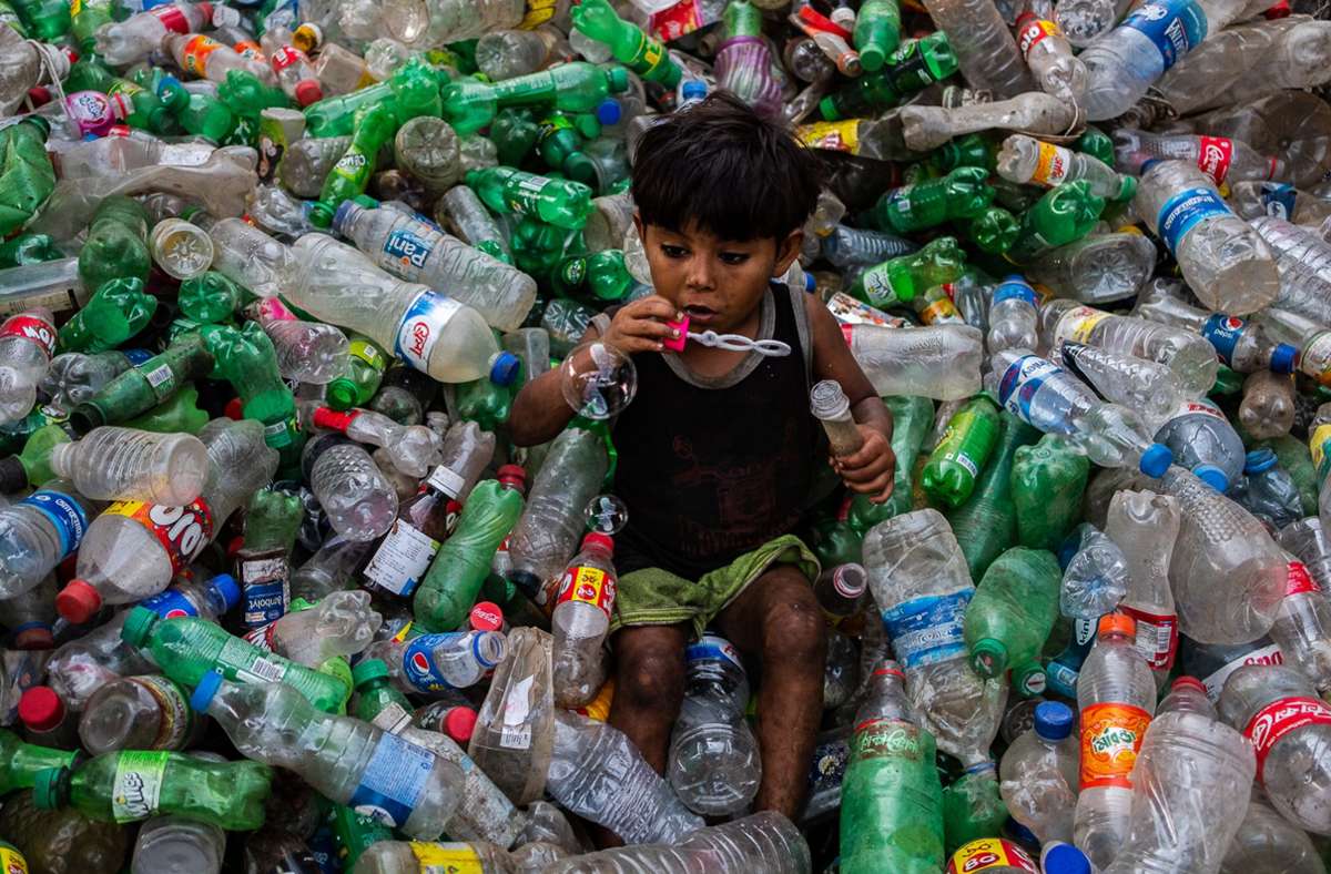 Ein Junge pustet Seifenblasen auf einem Stapel von Plastikflaschen in einer Recycling-Anlage in Dhaka (Bangladesch). Foto: Nayem Shaan/ZUMA Wire/dpa
